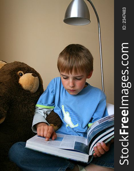 A small boy is reading interesting book with his teddy bear. A small boy is reading interesting book with his teddy bear