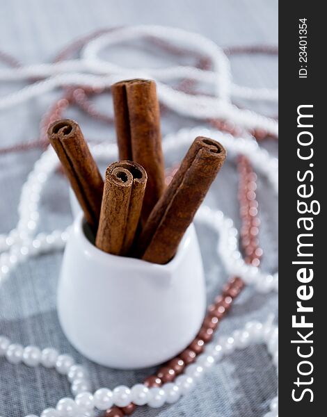 Cinnamon sticks in a white glass, beads on a blue background. Cinnamon sticks in a white glass, beads on a blue background