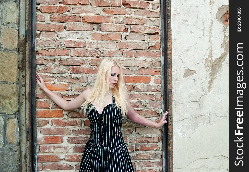 Blonde gothic girl in front of a brick wall in a striped black dress. Blonde gothic girl in front of a brick wall in a striped black dress