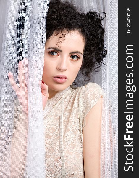 Closeup shot of brunette model wearing lace vintage blouse standing and peeking past a sheer curtain. Closeup shot of brunette model wearing lace vintage blouse standing and peeking past a sheer curtain