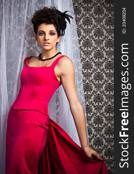 Brunette model wearing vintage/victorian red dress and black pearl necklace in front of sheer curtain. Brunette model wearing vintage/victorian red dress and black pearl necklace in front of sheer curtain