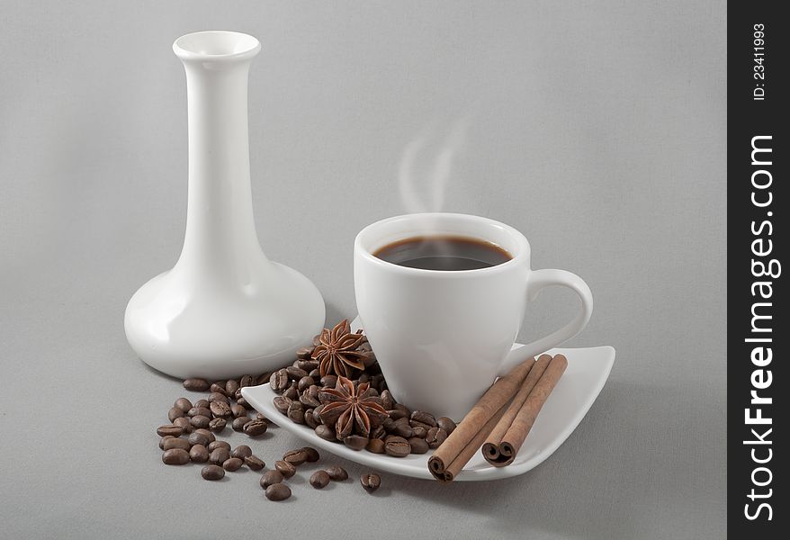 Black coffee in a white mug stands on a saucer with the spilled grains on a background a white vase. Black coffee in a white mug stands on a saucer with the spilled grains on a background a white vase
