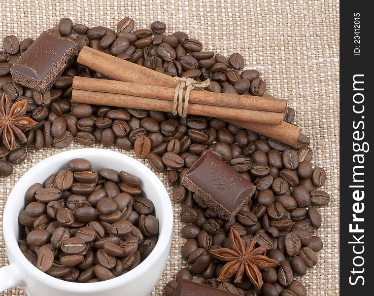 Grains of coffee, chocolate, anise, cinnamon and mug with bobs on a background sacking