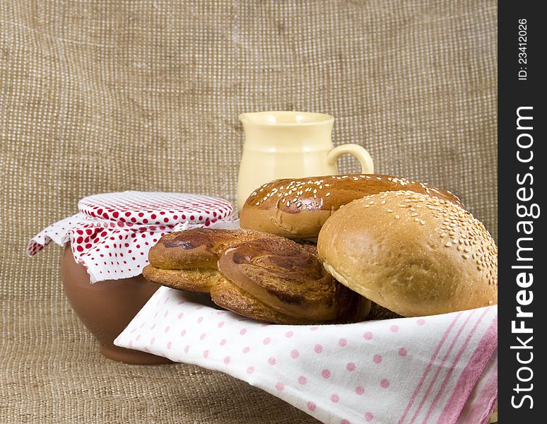 Panary rolls lie on a napkin in a basket on a background a pot from clay and jug