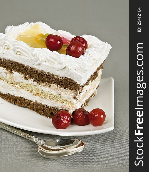 Piece of cake with a cherry and air cream on a grey background. Piece of cake with a cherry and air cream on a grey background