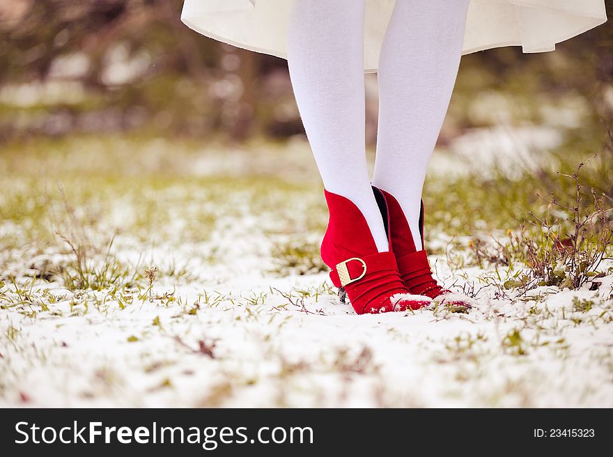 Part of feet in red shoes and white stockings on a grass and snow