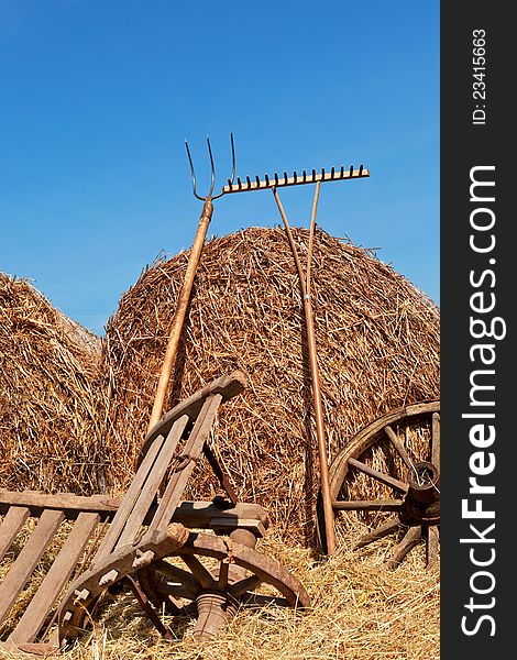 Traditional agriculture background. Hay bales, wooden wheel and wooden antique wheelbarrow against blue sky.