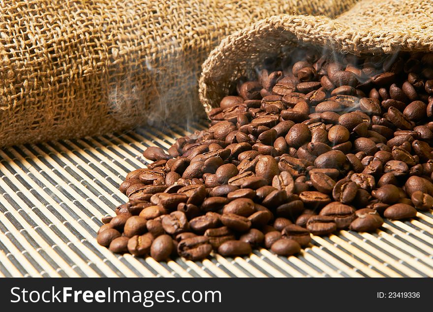 Fried grains of coffee with a smoke poured out a bag on a wooden napkin. Fried grains of coffee with a smoke poured out a bag on a wooden napkin