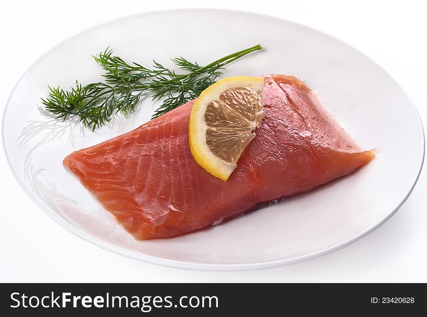 Fillet of red fish with a lemon and greens on a plate isolated on a white background