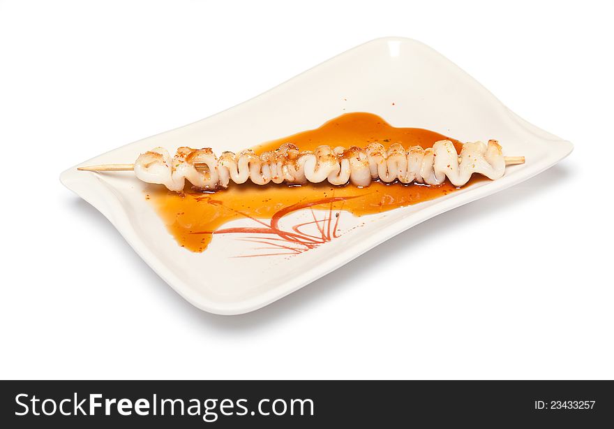 Skewered squid on wooden sticks grilled with sauce on a white plate on white background