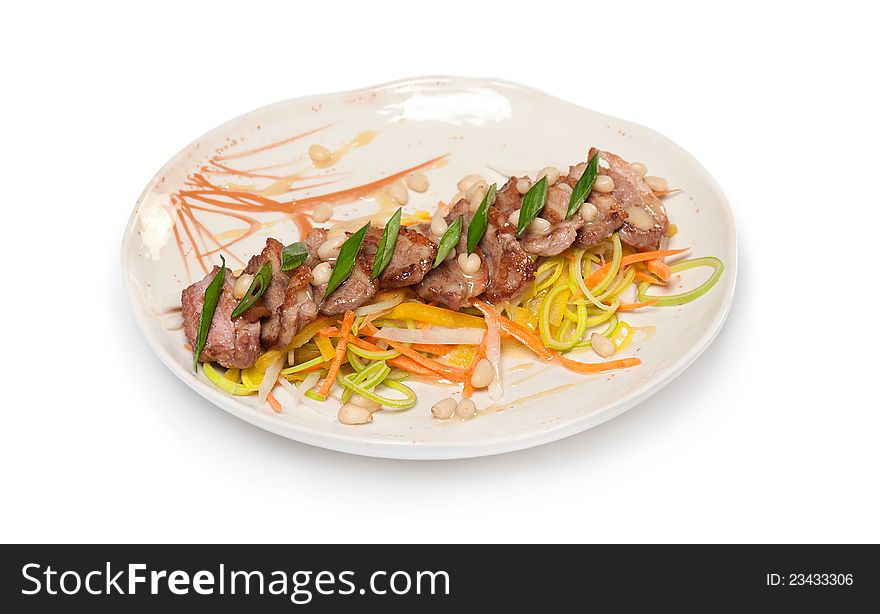 Fried beef with sauce, green onions, vegetables, pine nuts on a white plate on white background