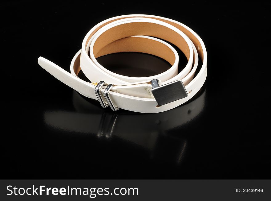 A womenâ€™s white leather belt with reflection on a black background. A womenâ€™s white leather belt with reflection on a black background