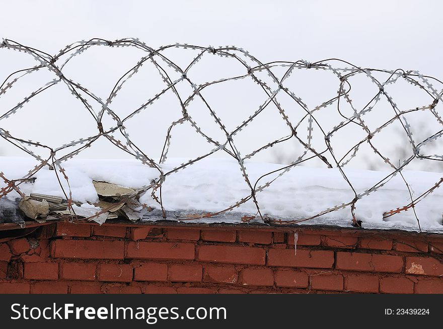 A brick fence with snow and barbed wire on top. A brick fence with snow and barbed wire on top