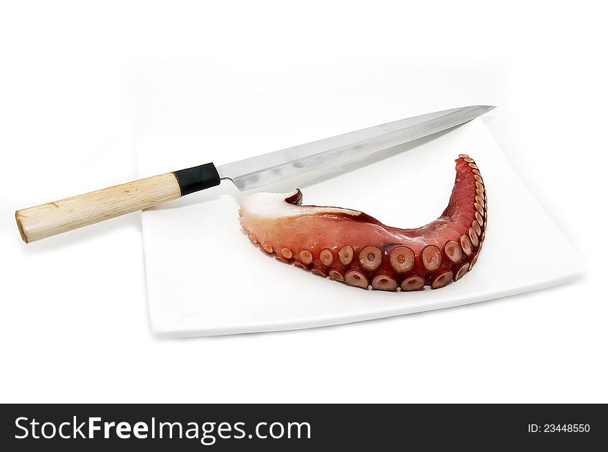 A piece of octopus on a plate and a knife on a white background