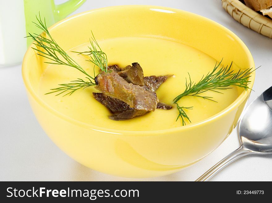 Yellow vegetable cream soup with meat on table