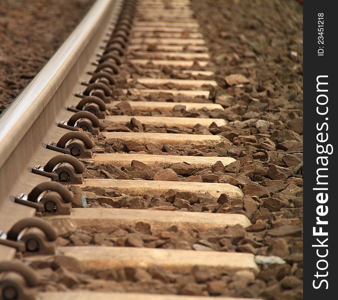 A low angle photo of a rusty railway track and it's tie downs.