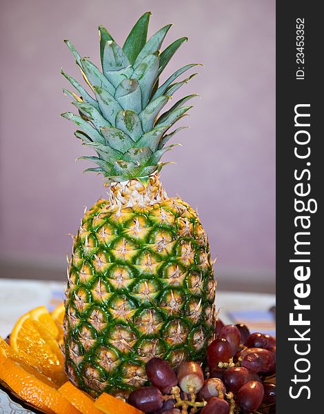 Pineapple with slices of oranges and grapes on table