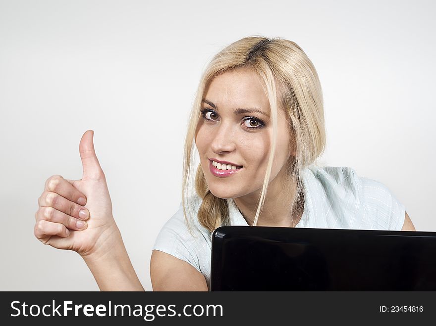 Beautiful happy girl sitting at a laptop computer and displays ok on the background of