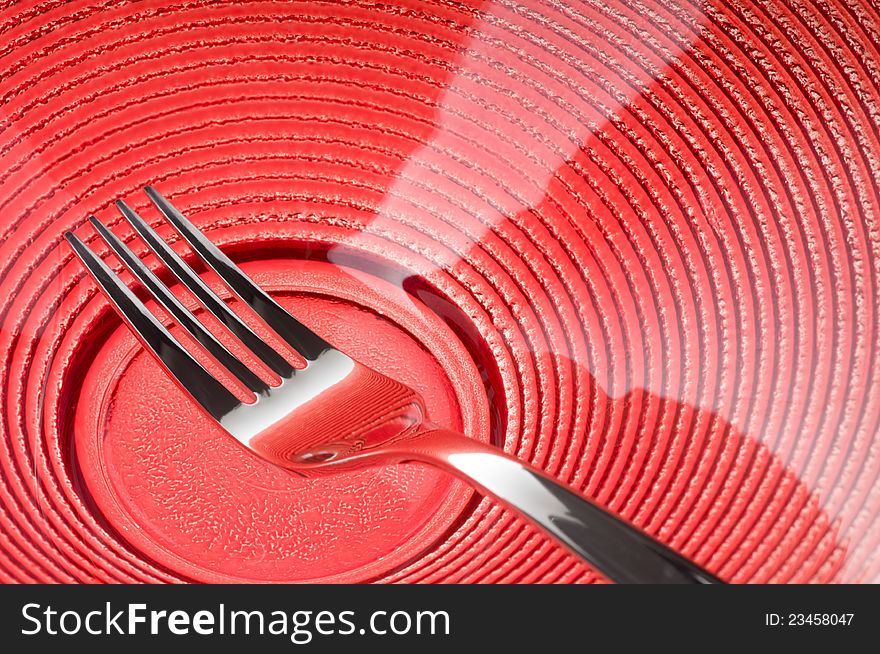 Metal fork over red plate. Metal fork over red plate