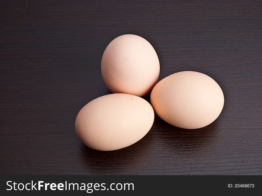 Three chicken eggs in a dark wooden background. Three chicken eggs in a dark wooden background