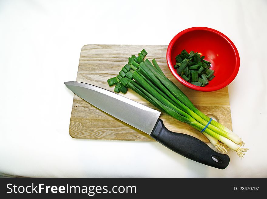 A cutting Board with a knife, bowl and a bunch of green onions. A cutting Board with a knife, bowl and a bunch of green onions