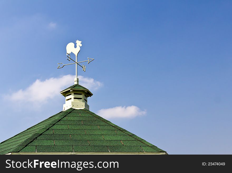 Rooster weather vane on roof and blue sky background