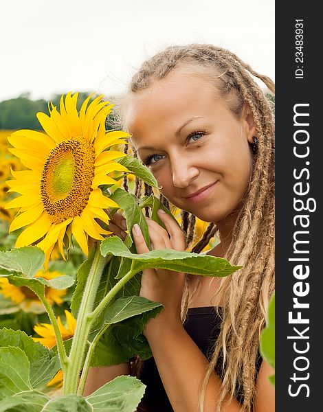Beautiful girl with dreadlocks posing next to the sunflower