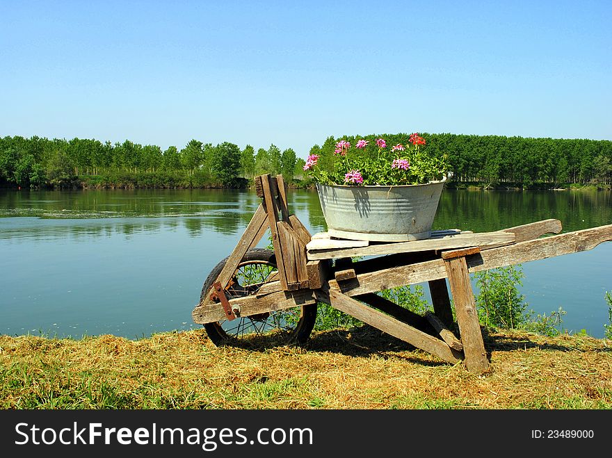 Old wooden wheel barrow with flowers close to river