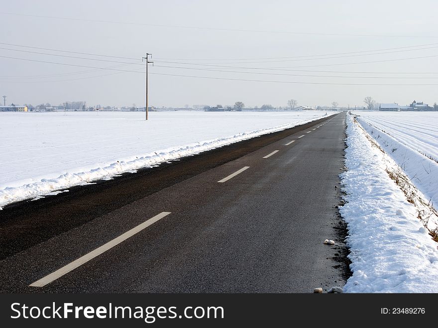 Asphalt street in a snow covered farmland landscape