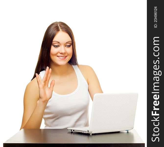 The young woman communicates  behind a table with the laptop on a white background. The young woman communicates  behind a table with the laptop on a white background