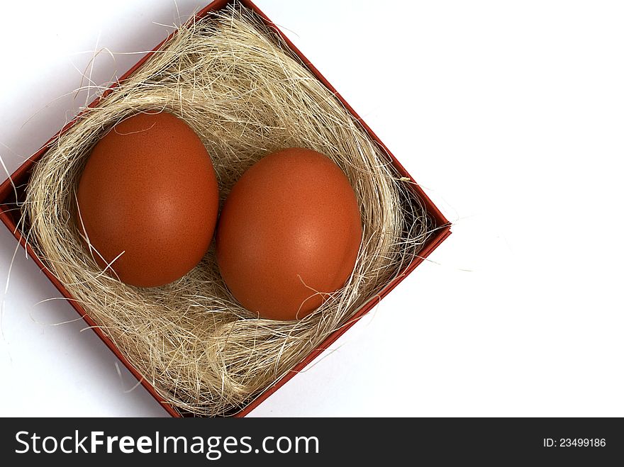 Two fresh brown eggs and some straw in a brown cardboard box on a white background. Two fresh brown eggs and some straw in a brown cardboard box on a white background