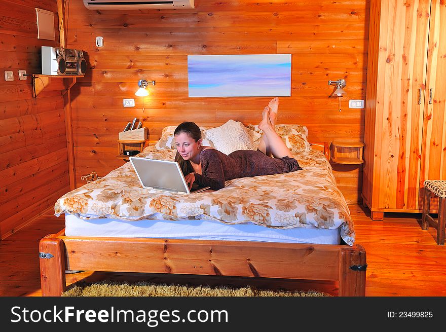 Girl with laptop lying on the bed in a rustic house and sends the mail to friends. Girl with laptop lying on the bed in a rustic house and sends the mail to friends