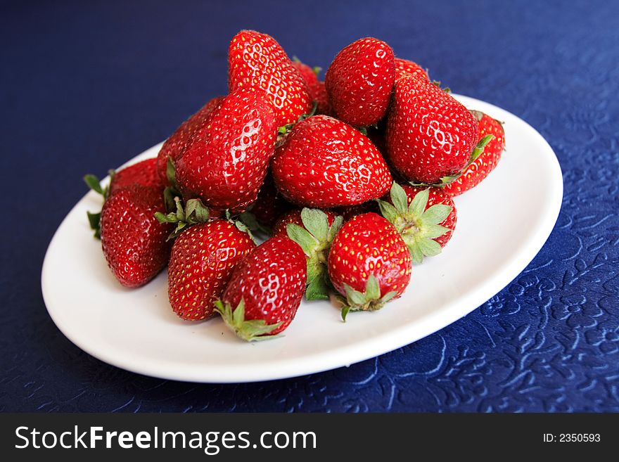 Hill of strawberries in white plate on a blue table-cloth