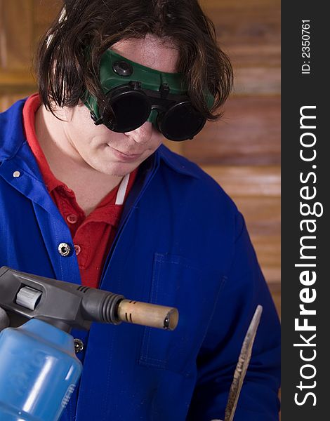 Dark haired man with blue overall holding blowtorch and metal. Dark haired man with blue overall holding blowtorch and metal