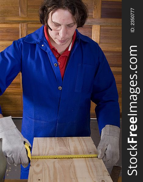 Dark haired man with blue overall measuring wood with gloves. Dark haired man with blue overall measuring wood with gloves