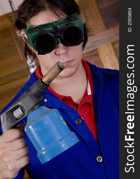 Dark haired man with blue overall holding blowtorch wearing welding goggles. Dark haired man with blue overall holding blowtorch wearing welding goggles