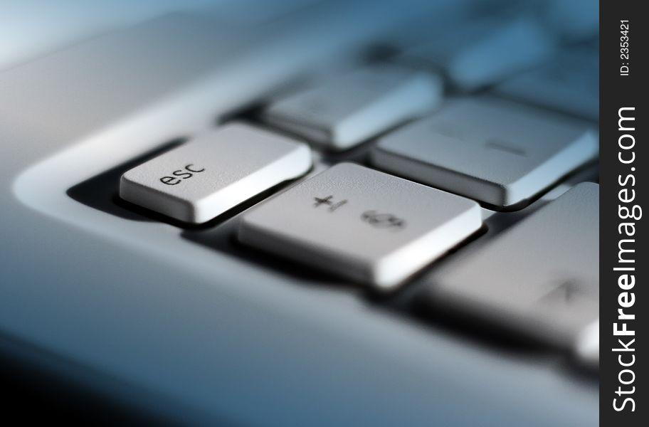 Close-up of laptop keyboard with focus on escape key. Blue lighting effect added with clear patch on escape key. Close-up of laptop keyboard with focus on escape key. Blue lighting effect added with clear patch on escape key.