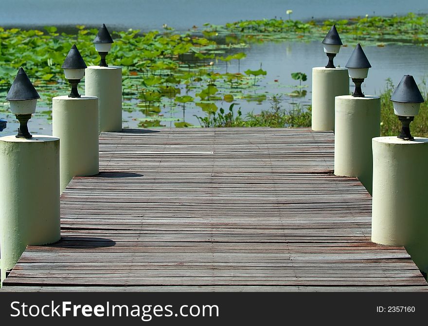 Wooden jetty with concrete lampposts at a lake. Shallow depth of field with foliage in the lake blurred