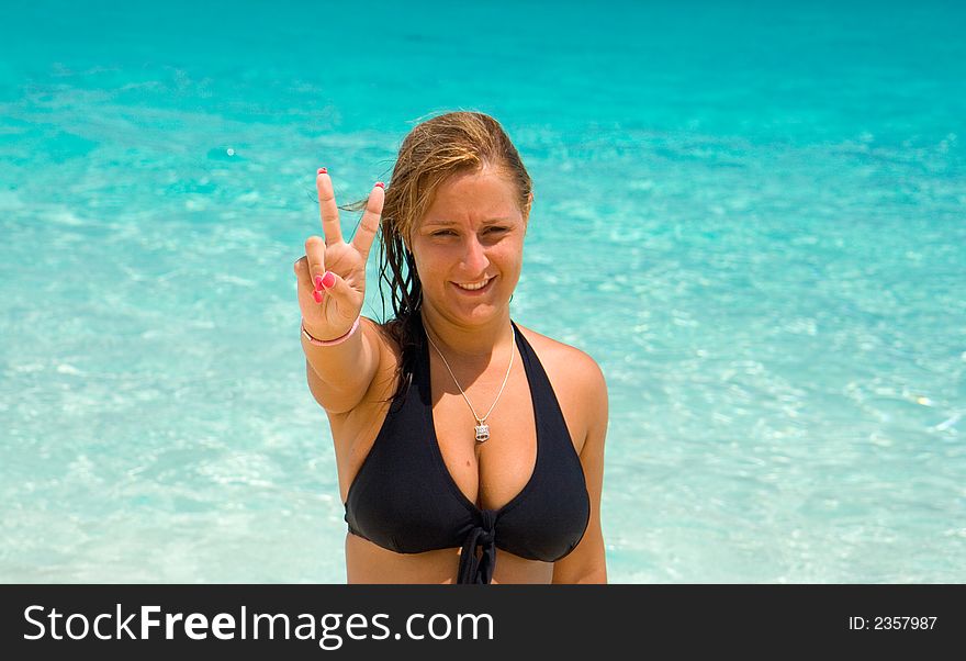 Young woman in black bikini showing the number two with the fingers of her right hand.  Background is of clear blue water. Young woman in black bikini showing the number two with the fingers of her right hand.  Background is of clear blue water.