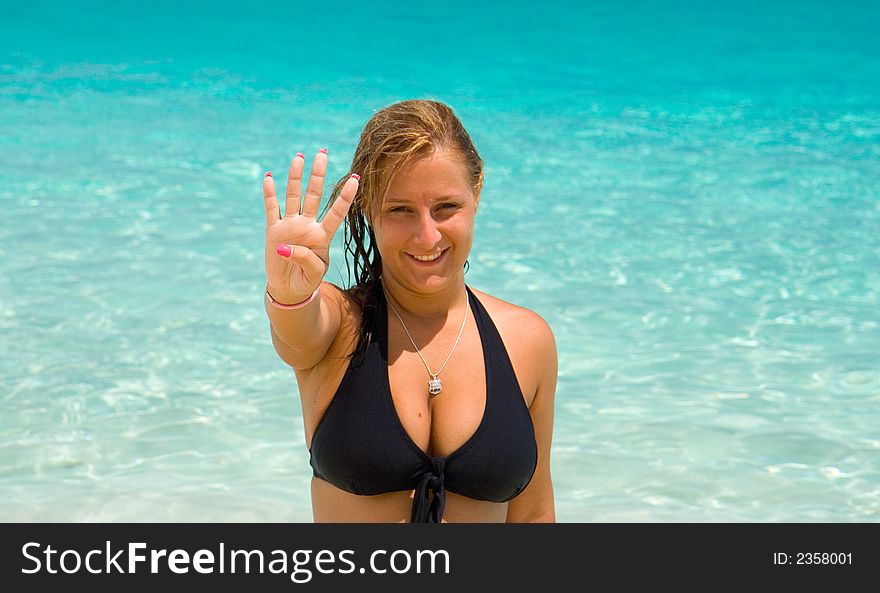 Young woman in black bikini showing the number four with the fingers of her right hand. Background is of clear blue water. Young woman in black bikini showing the number four with the fingers of her right hand. Background is of clear blue water.