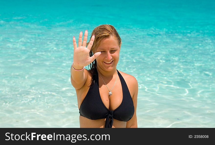 Young woman in black bikini showing the number five with the fingers of her right hand. Background is of clear blue water. Young woman in black bikini showing the number five with the fingers of her right hand. Background is of clear blue water.