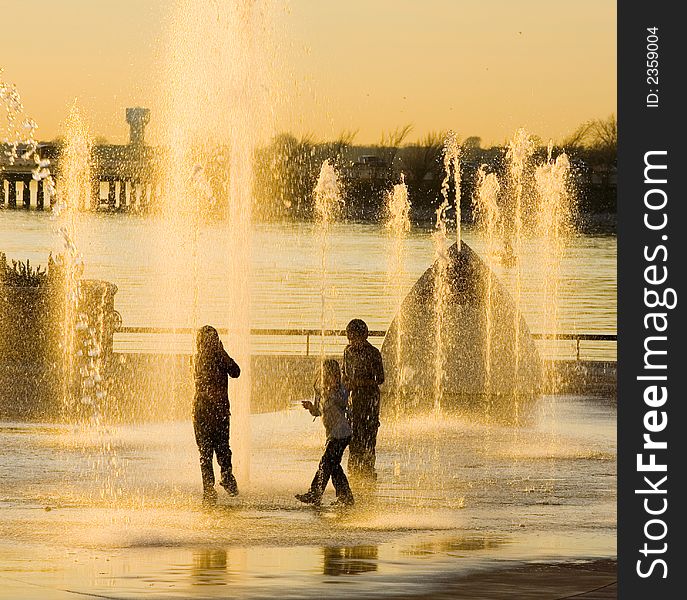 Three kids cool of in water fountain at sunset, no faces visable. Three kids cool of in water fountain at sunset, no faces visable