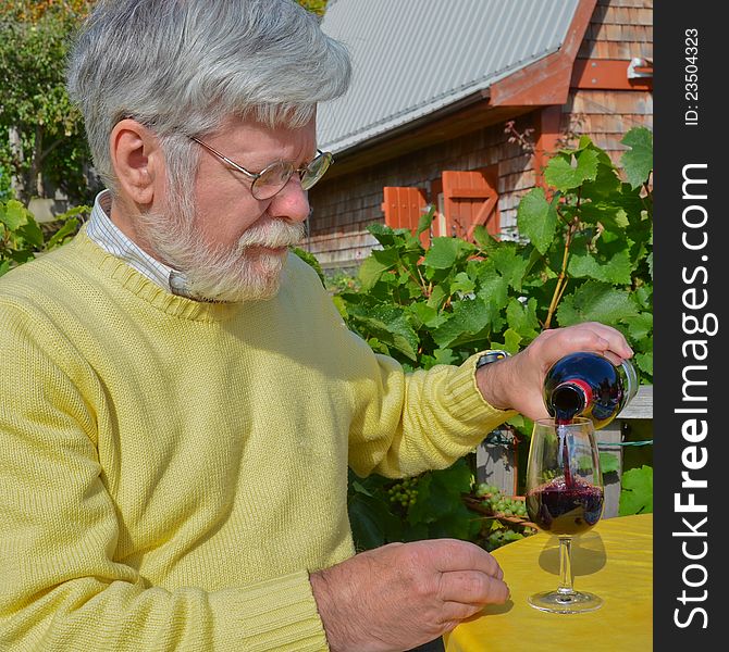 A senior male pours a glass of red wine in a vineyard on a sunny, fall day. A senior male pours a glass of red wine in a vineyard on a sunny, fall day