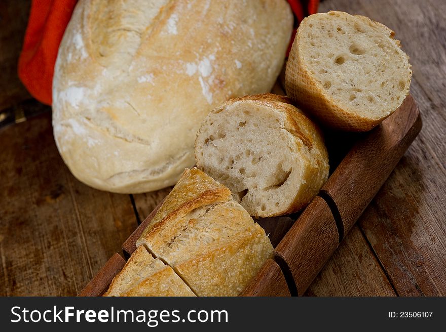 Freshly baked baguette sliced on a wooden bread cutting tray.  There is a second loaf of bread in the background. Freshly baked baguette sliced on a wooden bread cutting tray.  There is a second loaf of bread in the background.