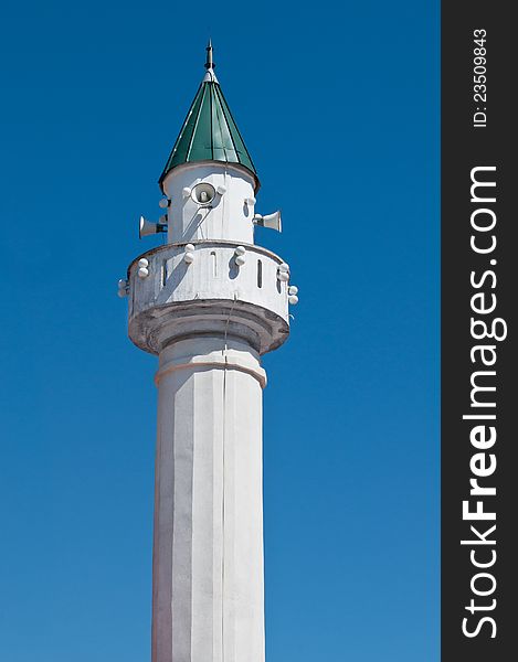 Small white minaret with green roof on blue sky