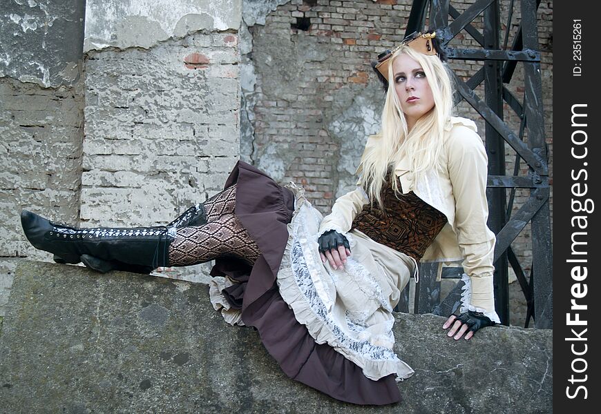 Steampunk blond girl with flight glasses on her had sitting on a concrete wall