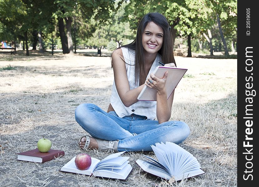 Young woman sitting on the grass and holding notebook photographed in  park. Young woman sitting on the grass and holding notebook photographed in  park