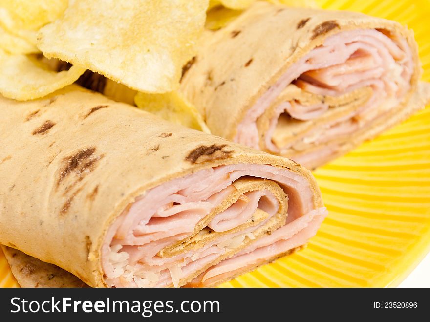 Rolled Sandwich with Chips on a yellow plate, up close.