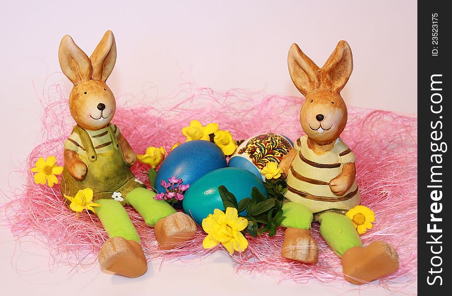 Toy rabbits are sitting near the dyed Easter eggs on a pink background. Toy rabbits are sitting near the dyed Easter eggs on a pink background