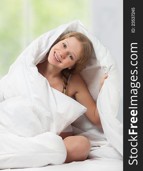 Funny beautiful young blond woman under the blanket in the bedroom with a window and green. Funny beautiful young blond woman under the blanket in the bedroom with a window and green